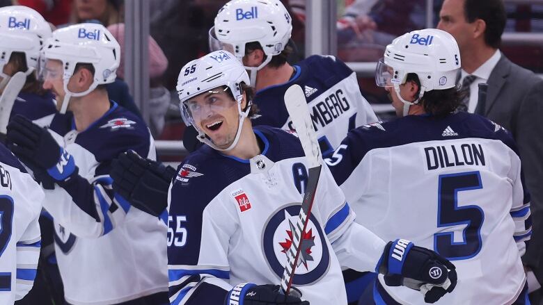 A hockey player smiles on the ice surrounded by his teammates.