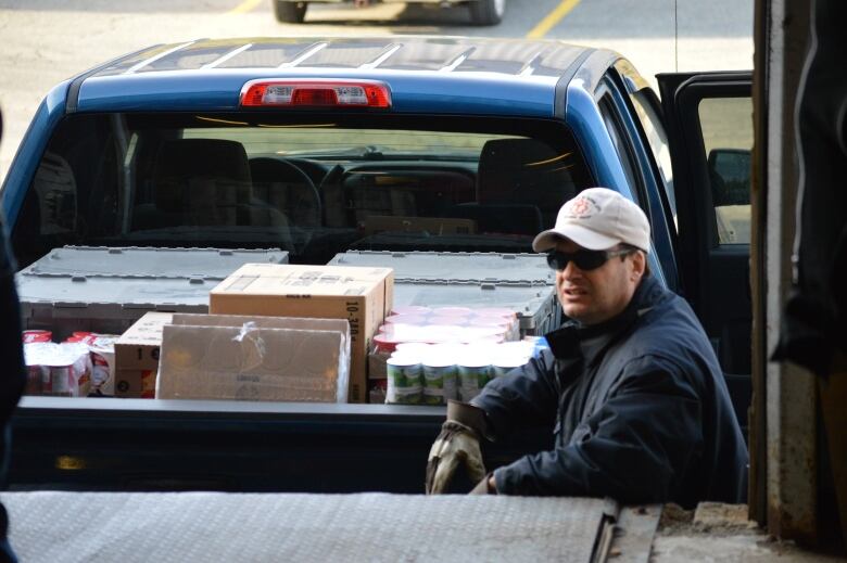 A man leans against a truck filled with canned goods