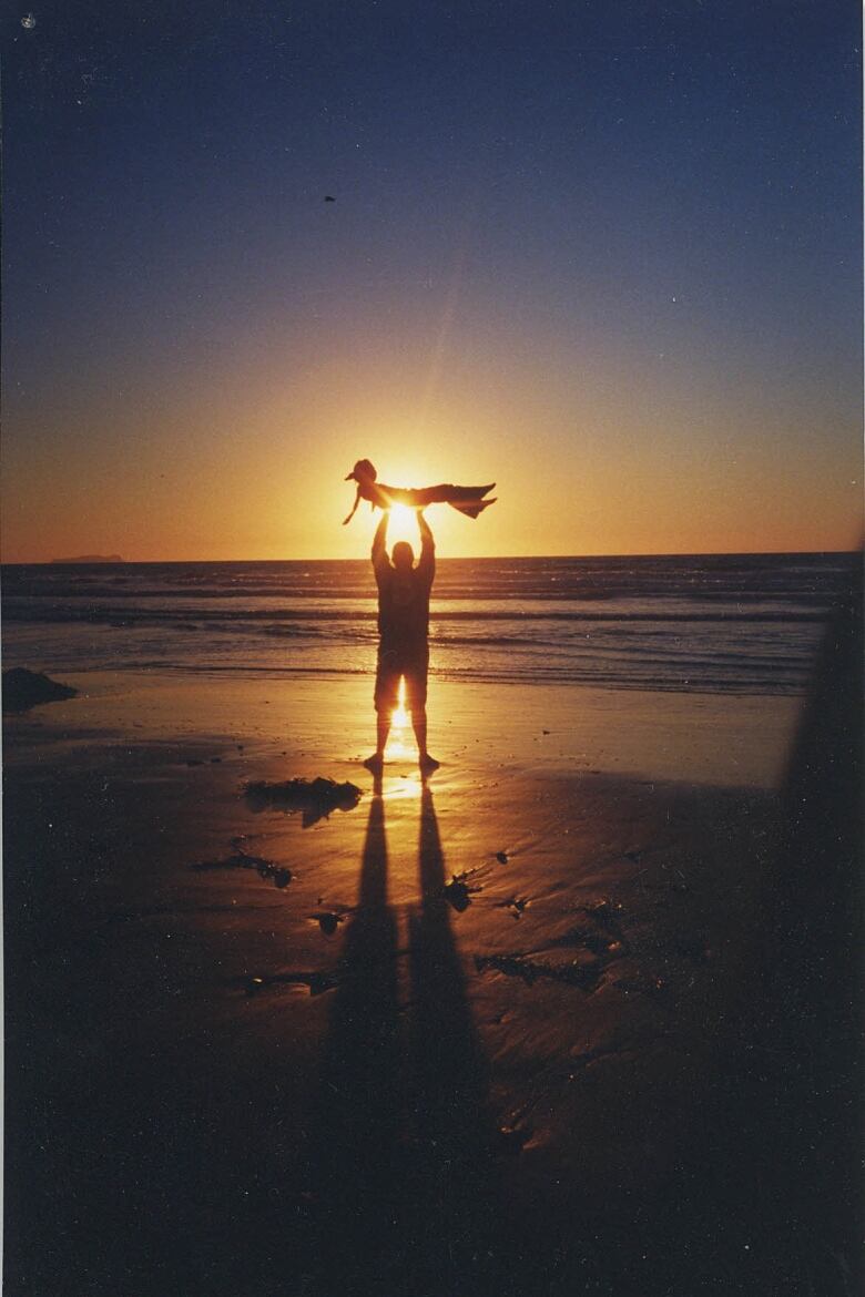 A man holds a kid over his head on a beach during sunset.