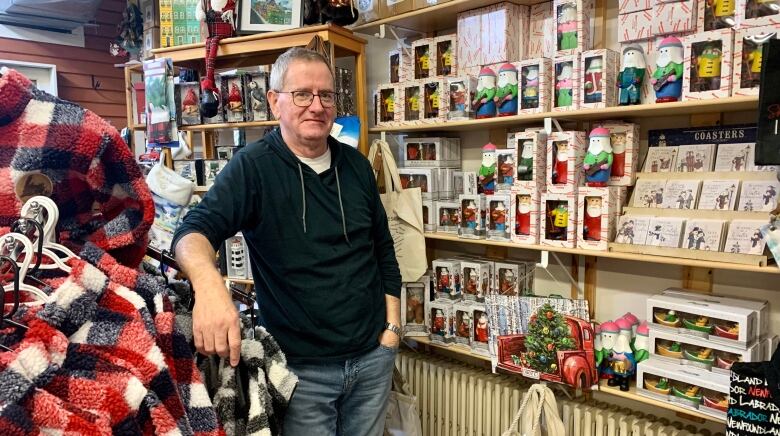 A man wearing a black sweater and jeans stands beside a display of Christmas souvenirs. 