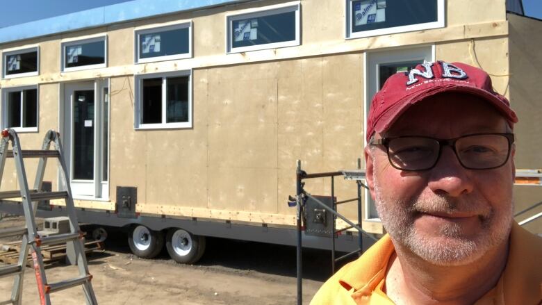 A man stands in front of a tiny home under construction.