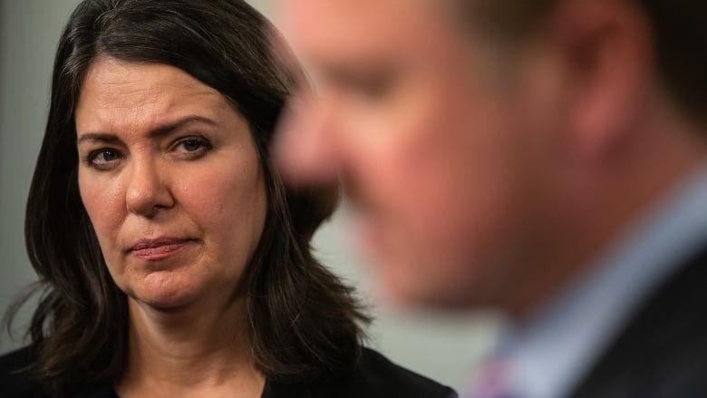 Closeup of Premier Danielle Smith, Justice Minister Tyler Shandro in the foreground blurred.