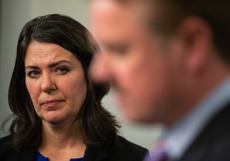 Closeup of Premier Danielle Smith, Justice Minister Tyler Shandro in the foreground blurred.