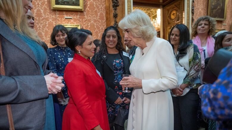 A white=haired woman at the centre of a group of woman in an ornate room. 