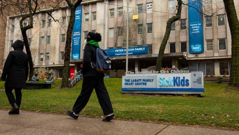 A sign of the SickKids Hospital sign, with people walking past it.