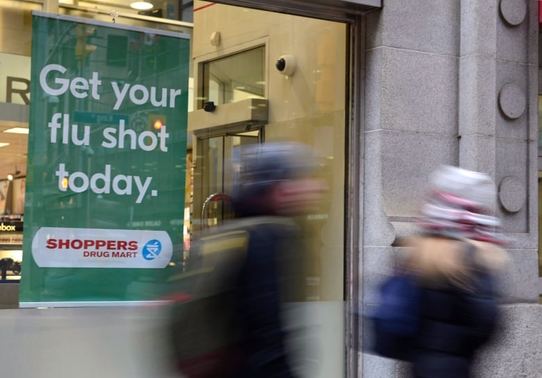 The blurred figures of two people are seen walking by a store window with a sign reading 