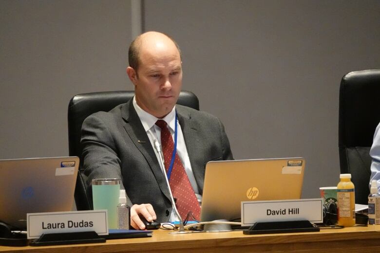 A politician at a desk with his nameplate uses a computer mouse.