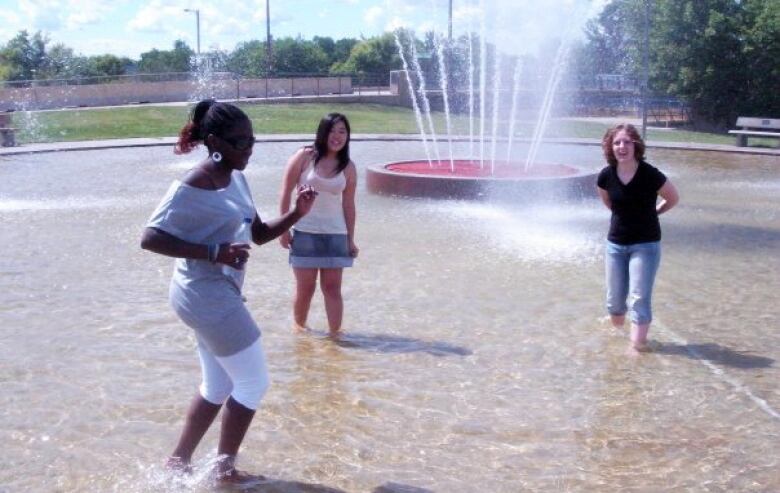 Three teenage girls wade in a splash pool.