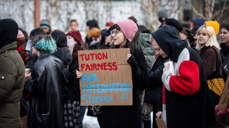 A young woman holds a sign that says tuition fairness for international students.