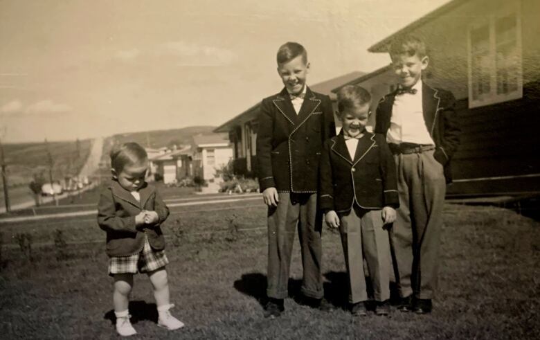 Three boys in suit jackets grin at the camera while a young boy off to the side examines his hands carefully. 