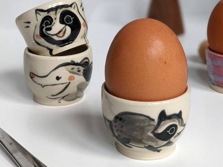 Photo of three illustrated ceramic eggcups featuring painted cartoons of possums and raccoons.