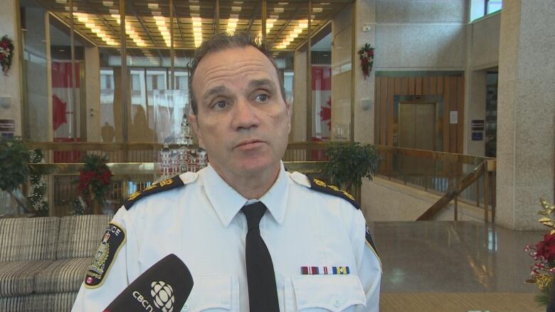 A man in a white uniform dress shirt and tie stands in a large indoor area with a CBC microphone directed to him.