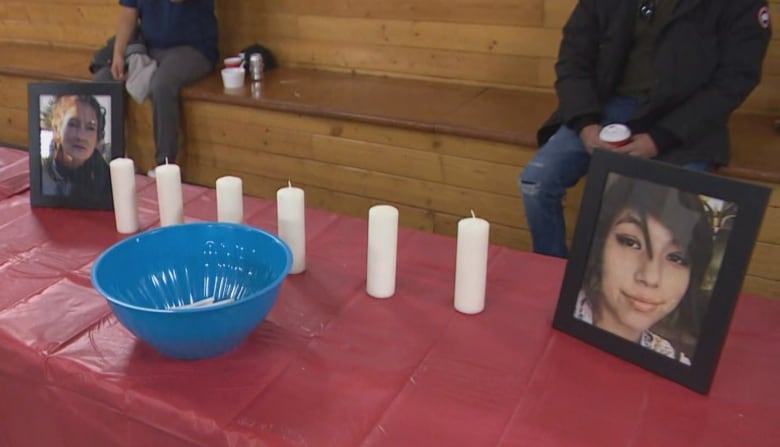 Framed photos of two women sit on a long table covered by a red plastic cloth, with six unlit candles sitting between them.