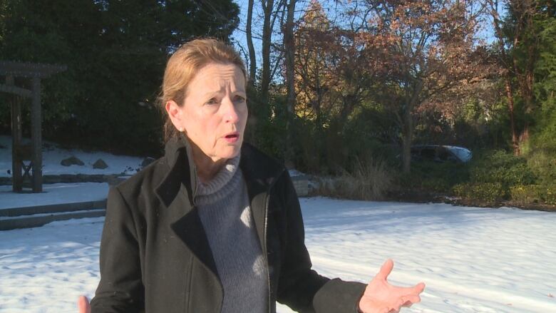 A woman standing outside with snow all around gestures with both hands as she speaks to a reporter.