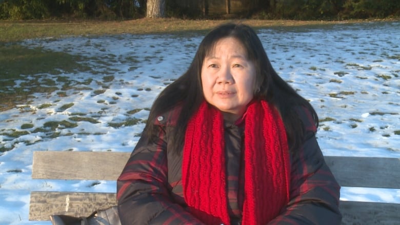 An East Asian woman with a red scarf sits on a park bench amid snowy conditions.