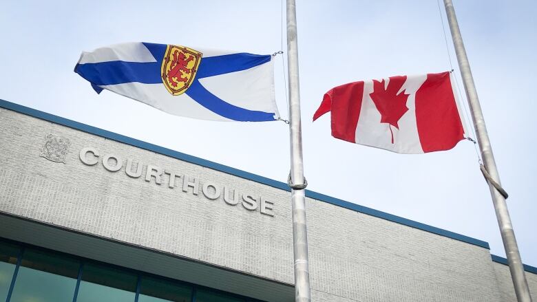 Nova Scotia and Canadian flags wave in the wind over the top of a brick building labelled courthouse.