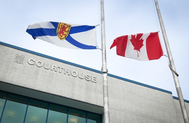 Nova Scotia and Canadian flags wave in the wind over the top of a brick building labelled courthouse.