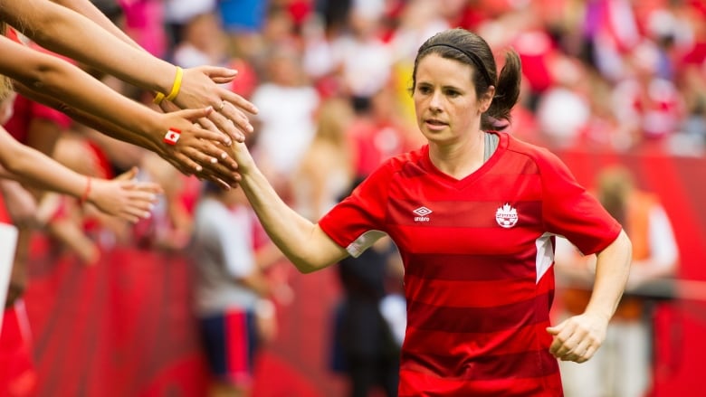 A soccer player in a red jersey high-fives fans.