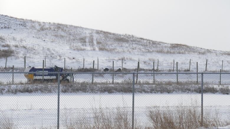 A garbage truck drives behind a fenced area covered in snow.