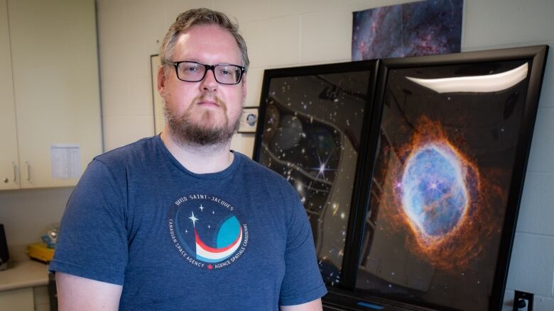 Person in a blue t-shirt poses for the camera with posters of galaxies and stars in the background.