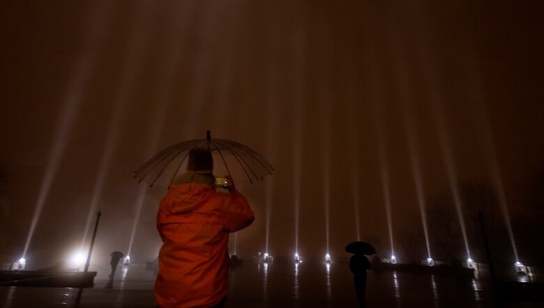 A person takes a photo of 14 beams of light in the rain.