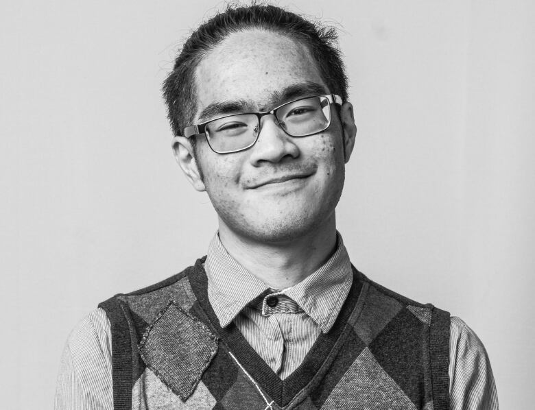 A young man with glasses, in a buttoned-up shirt and vest, smiles at the camera.