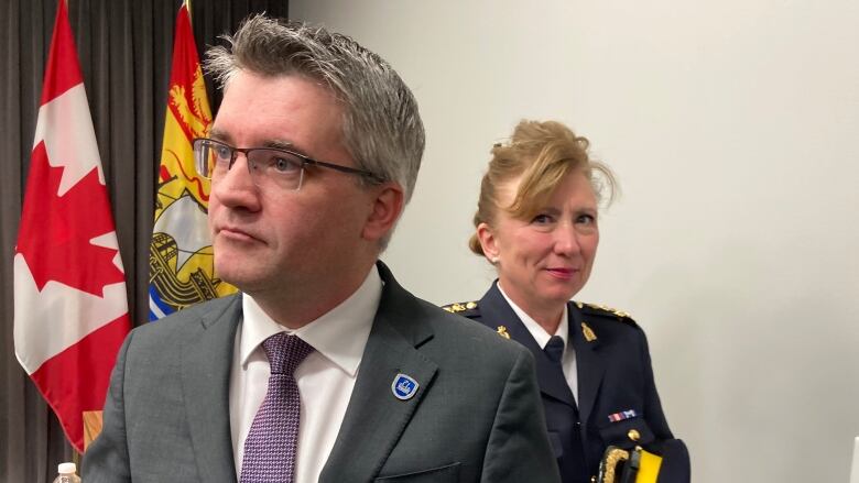 A man in a grey suit with glasses and a woman in an RCMP uniform at a news conference.