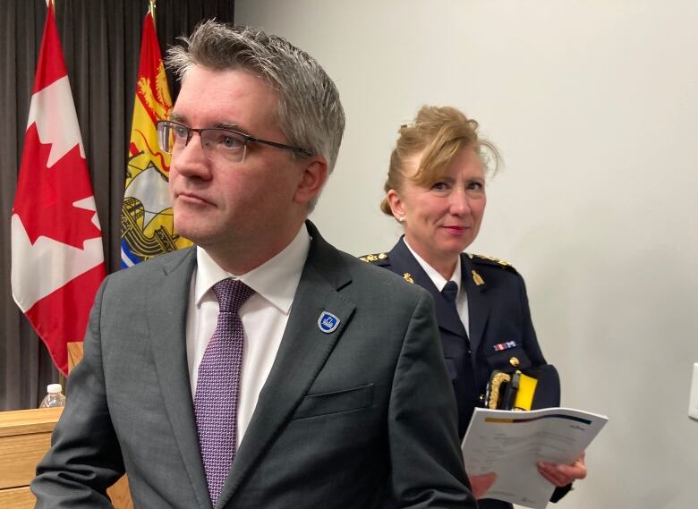 A man in a grey suit with glasses and a woman in an RCMP uniform at a news conference.