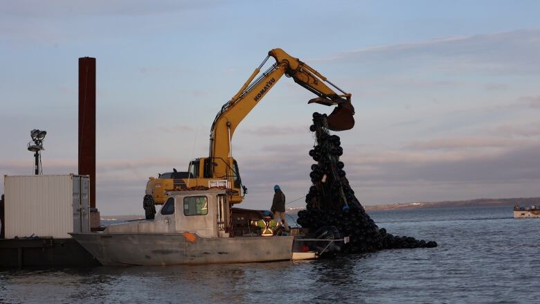 A crane on a barge lifts a giant tangle of ropes and buoys. 