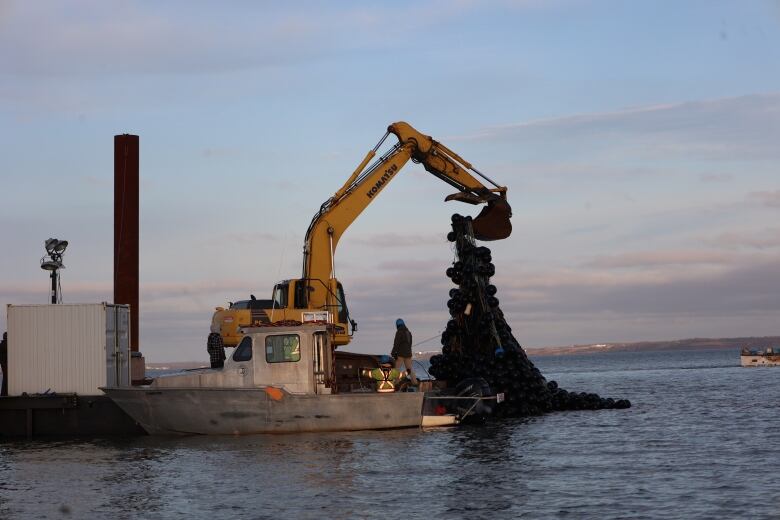 A crane on a barge lifts a giant tangle of ropes and buoys. 