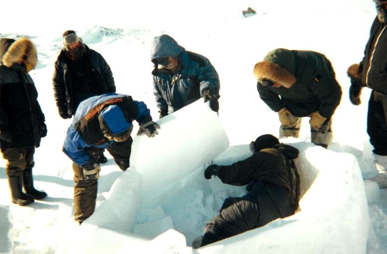 A group of people help move large blocks of ice into a circle shape.