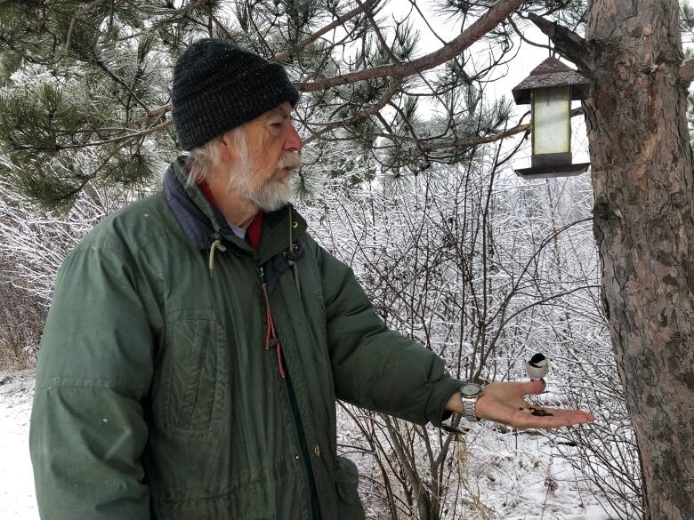 A man standing outside in the winter with a chickadee eating out of his hand.