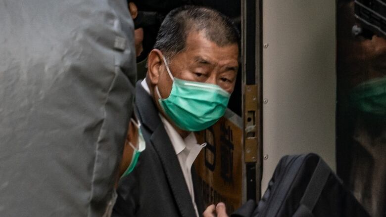 Close-up of a man, Jimmy Lai, surrounded by people going into a building.