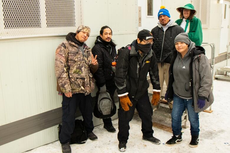 A group of people stand on and in front of the steps leading to a white, aluminum-sided building, made from a converted shipping container.