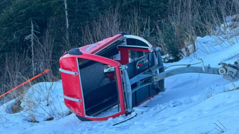 Red ski gondola lying on its side in snow.