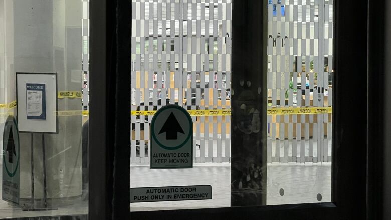 Police tape is seen through some glass doors. Behind the tape is a barricade in a library.