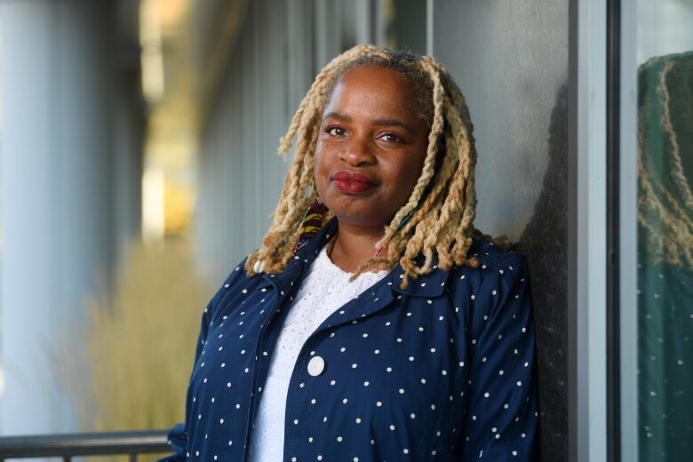 A woman leans against a wall and smiles at the camera for this portrait photo.