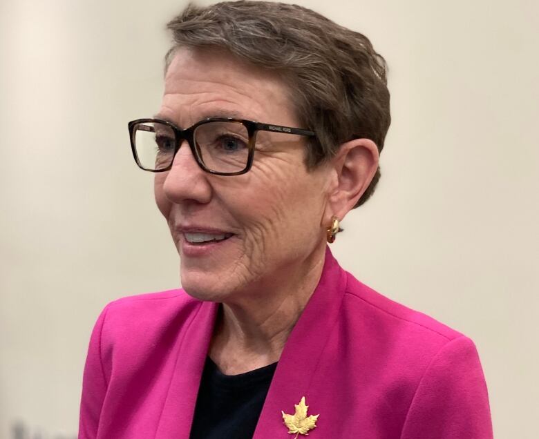 A woman with brown hair and glasses in a pink blazer.