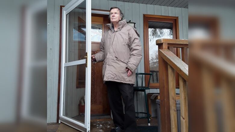 A man in jacket stands on the porch in front of the house's main entrance.