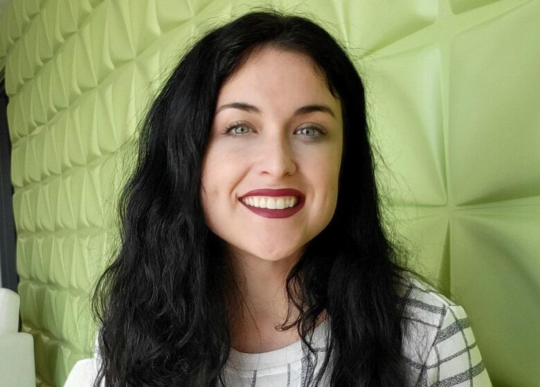 A woman sitting with a green background. 