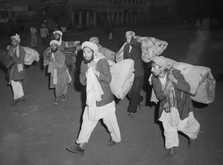 Afghan traders are walking with their belongings at night through the streets in this black and white image.