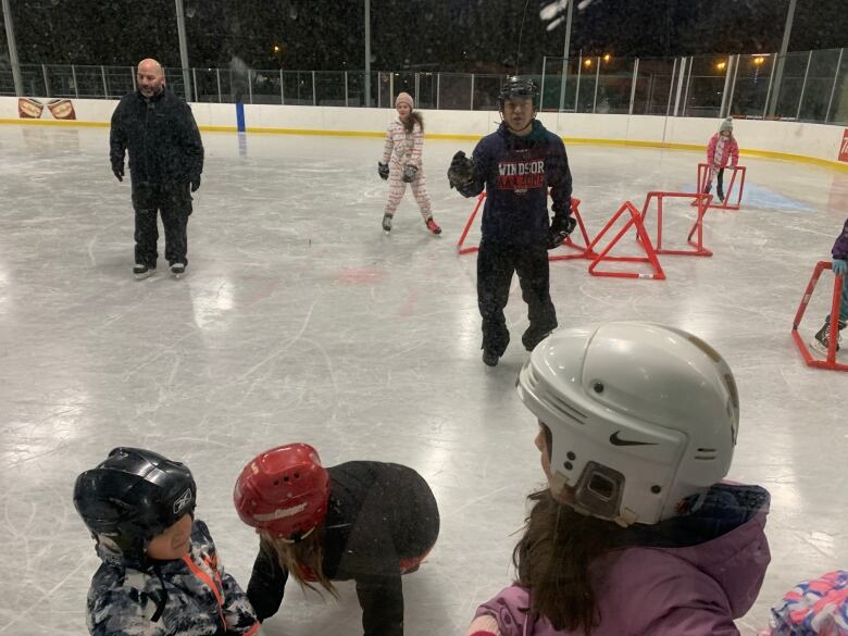 Man in skates and a helmet giving instructions to a group of young kids on how to skate