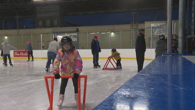 Two children hold a skating device to keep themselves steady on the ice