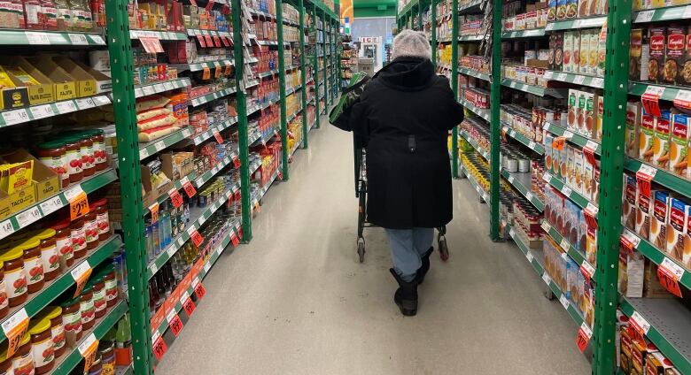 A woman wearing winter clothes pushes a cart down a grocery store aisle