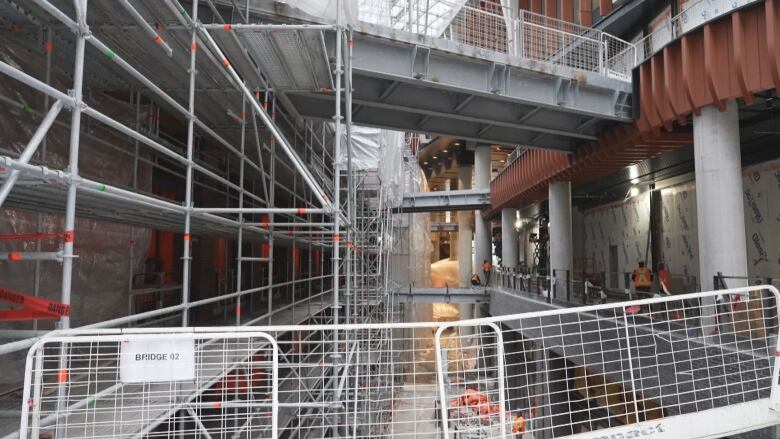 Scaffolding against the walls of an open-air, four-level tunnel. In the picture viewer can see bridges connecting the left side of the tunnel to the right.