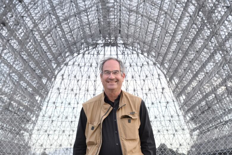 Man stands in the center of a large grey archway, which is the Moffett Federal Airfield in California.