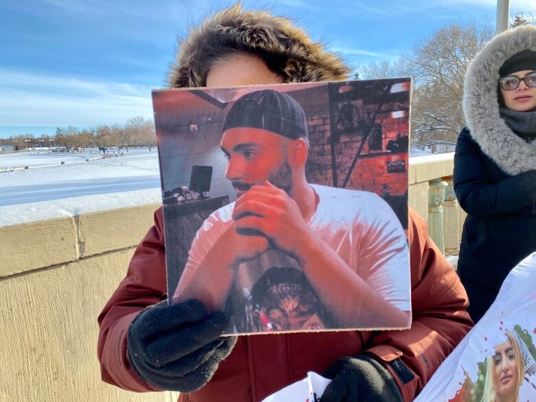 A woman in a fur hood holds a photo of a man during a protest on a bridge