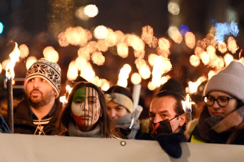 Four people, including one with her face painted, march in a rally while holding torches