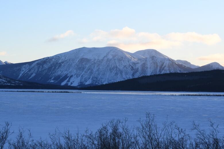 Golden light hits the edge of a snow-covered mountain rage. A mostly-frozen lake, also largely snow-covered, is in the foreground.