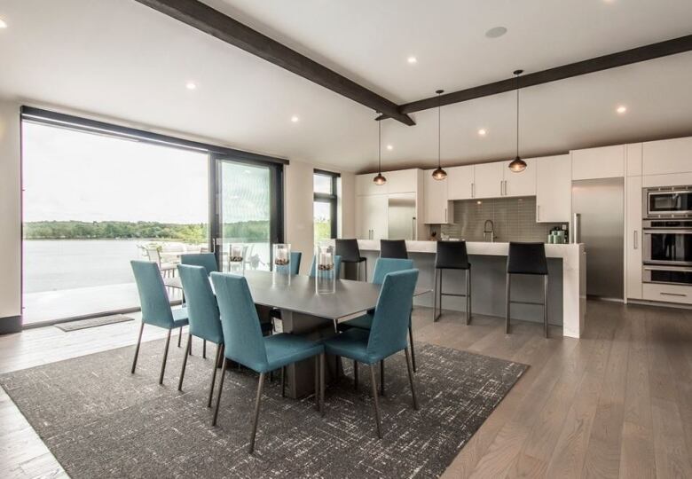 A dining room and kitchen combo. There is a large dining table in front of a kitchen island that has four barstool seats. There is a large window overlooking a lake at the end of the table on the left side.